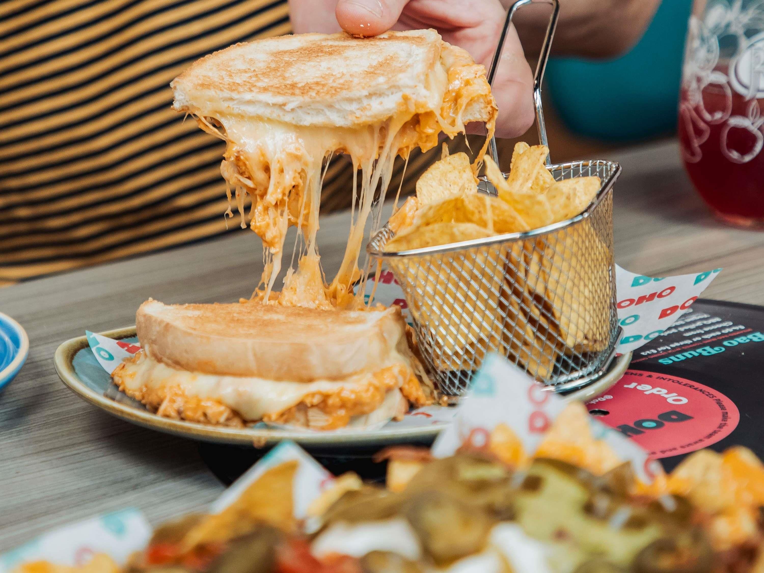 A grilled cheese sandwich with melted cheese being lifted by a fork, placed on a plate with a paper liner.