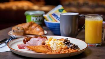 A breakfast plate with eggs, beans, ham, and a croissant, a mug, and a glass of orange juice on a table.