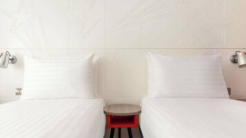 A hotel room with two beds, a small red stool, and wall-mounted lamps.