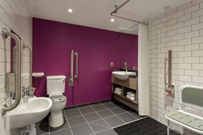 A modern bathroom with a purple wall, white fixtures, and a shower area. - Ibis Styles Glasgow Central (Glasgow)