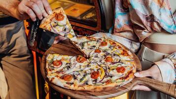 A person holding a pizza with toppings like tomatoes, onions, and peppers.