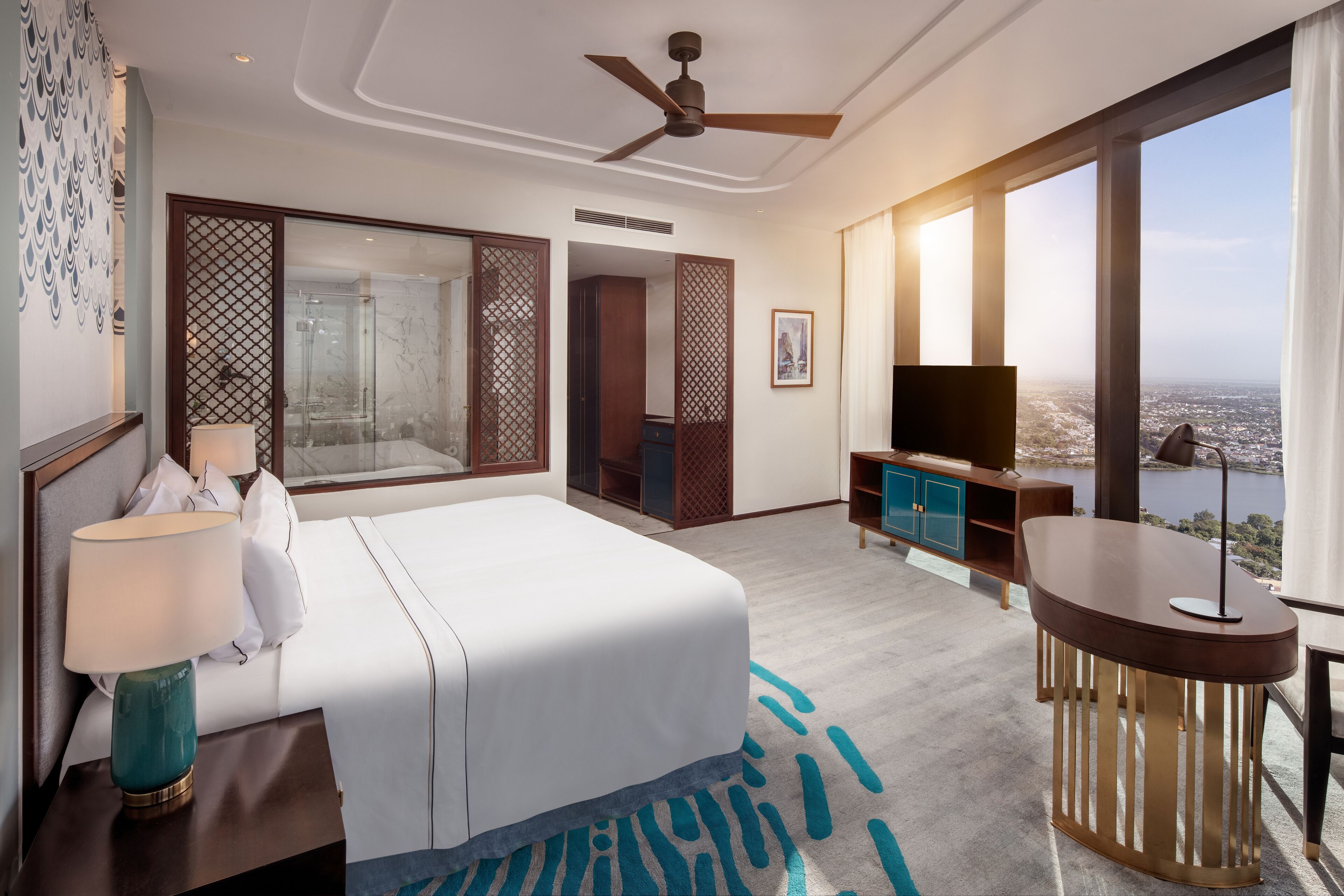 Una habitación de hotel con cama, escritorio, televisión y un ventanal con vista a la ciudad.