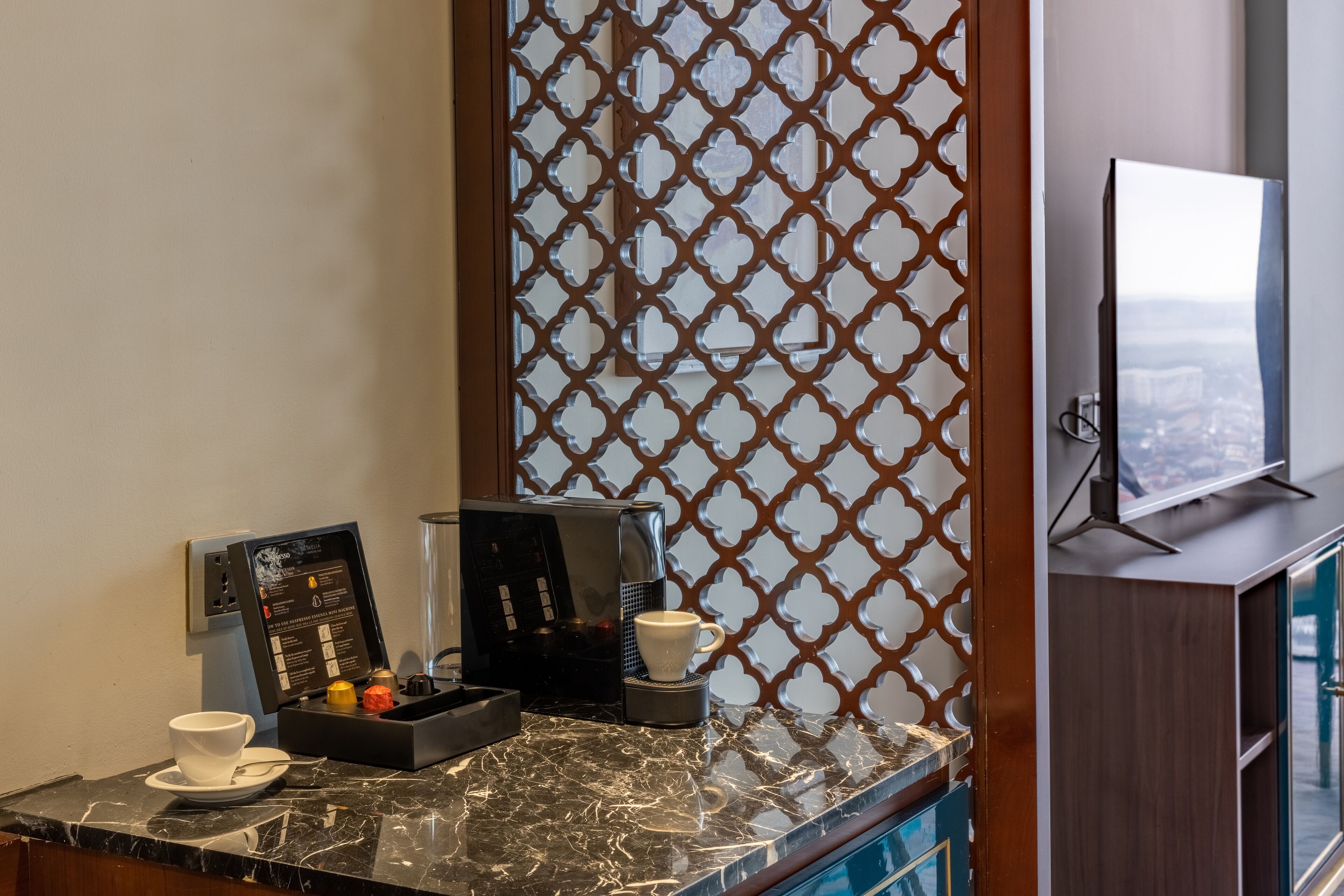 A hotel room with a coffee machine, a cup, and a tray of chocolates on the counter.
