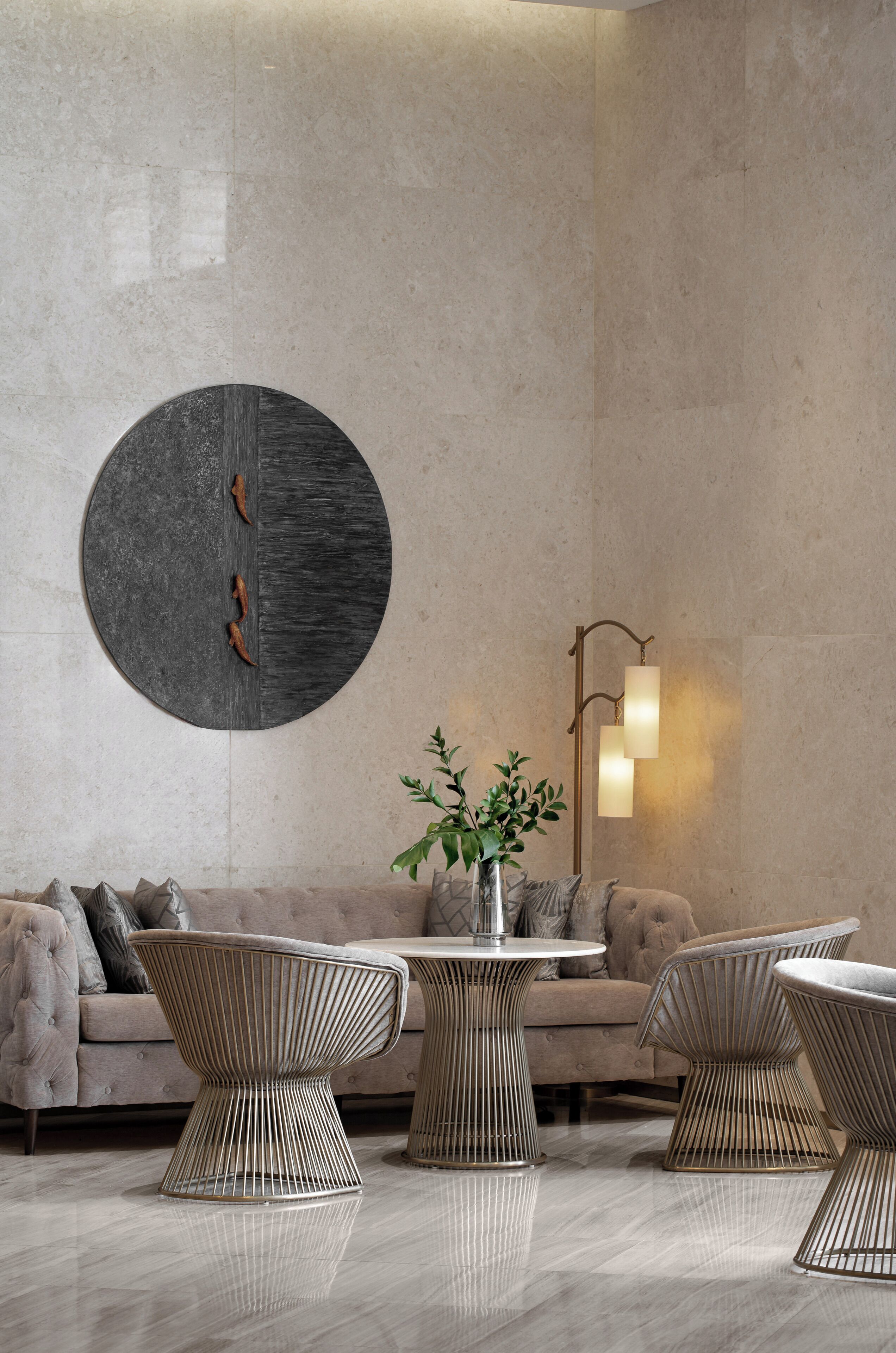 A modern interior with a round wall art piece, a table with a vase of green plants, and a sofa with cushions.