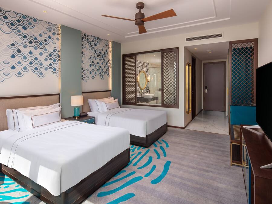 Habitación de hotel con dos camas, ventilador de techo, un espejo grande, televisión y baño con ducha.