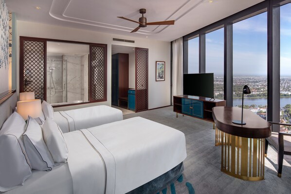Una habitación de hotel moderna con una cama grande, televisión y vistas a un paisaje urbano a través de amplios ventanales.