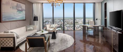 Ein geräumiges Wohnzimmer mit großem Fenster und Blick auf die Stadt, einem modernen Kronleuchter und einem Flachbildfernseher.