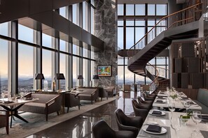 Un moderno vestíbulo de hotel con una larga mesa de comedor, asientos cómodos, una columna de mármol y una escalera.