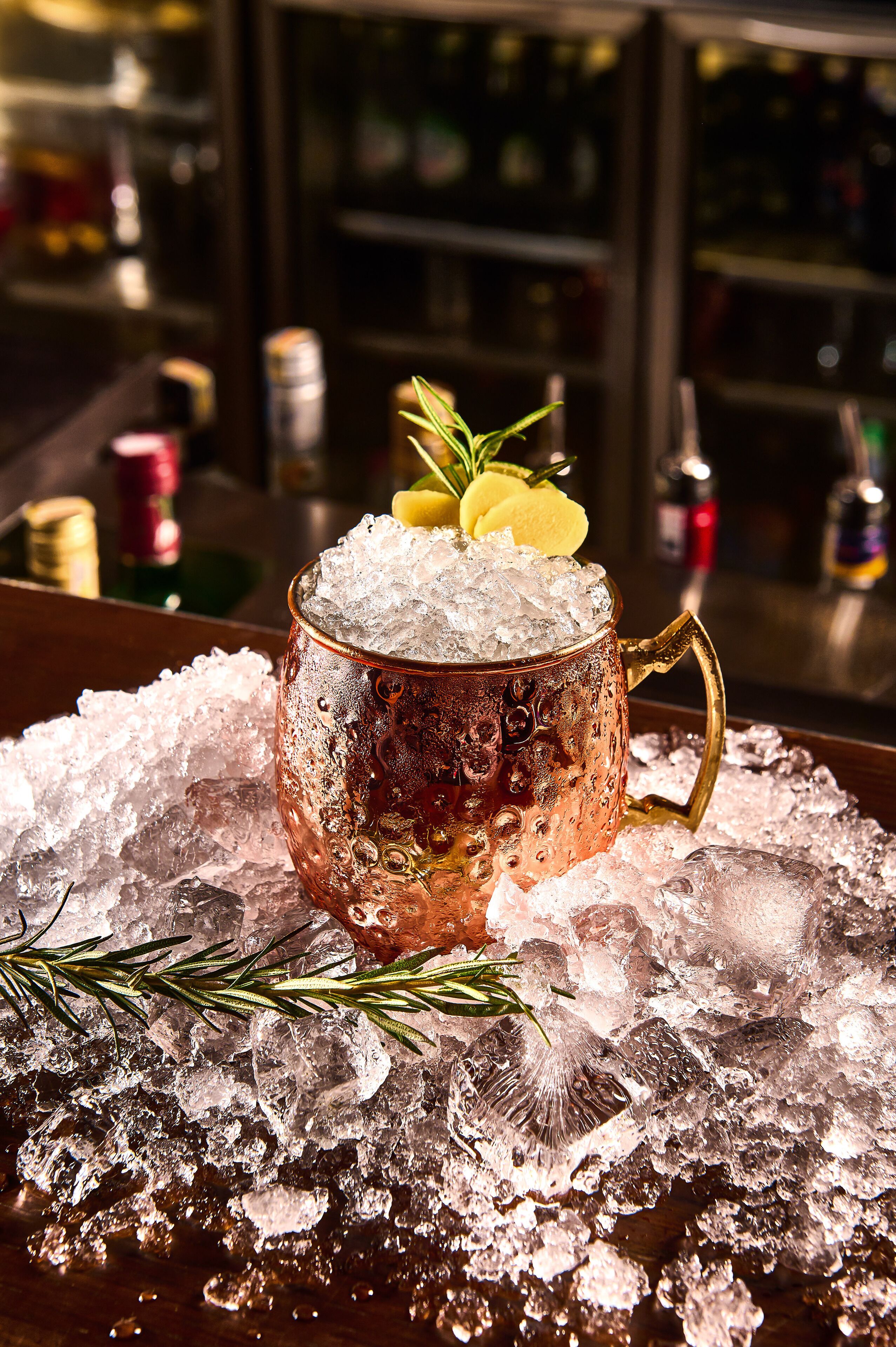 A copper mug filled with ice and garnished with rosemary and lemon slices, placed on a bed of ice.