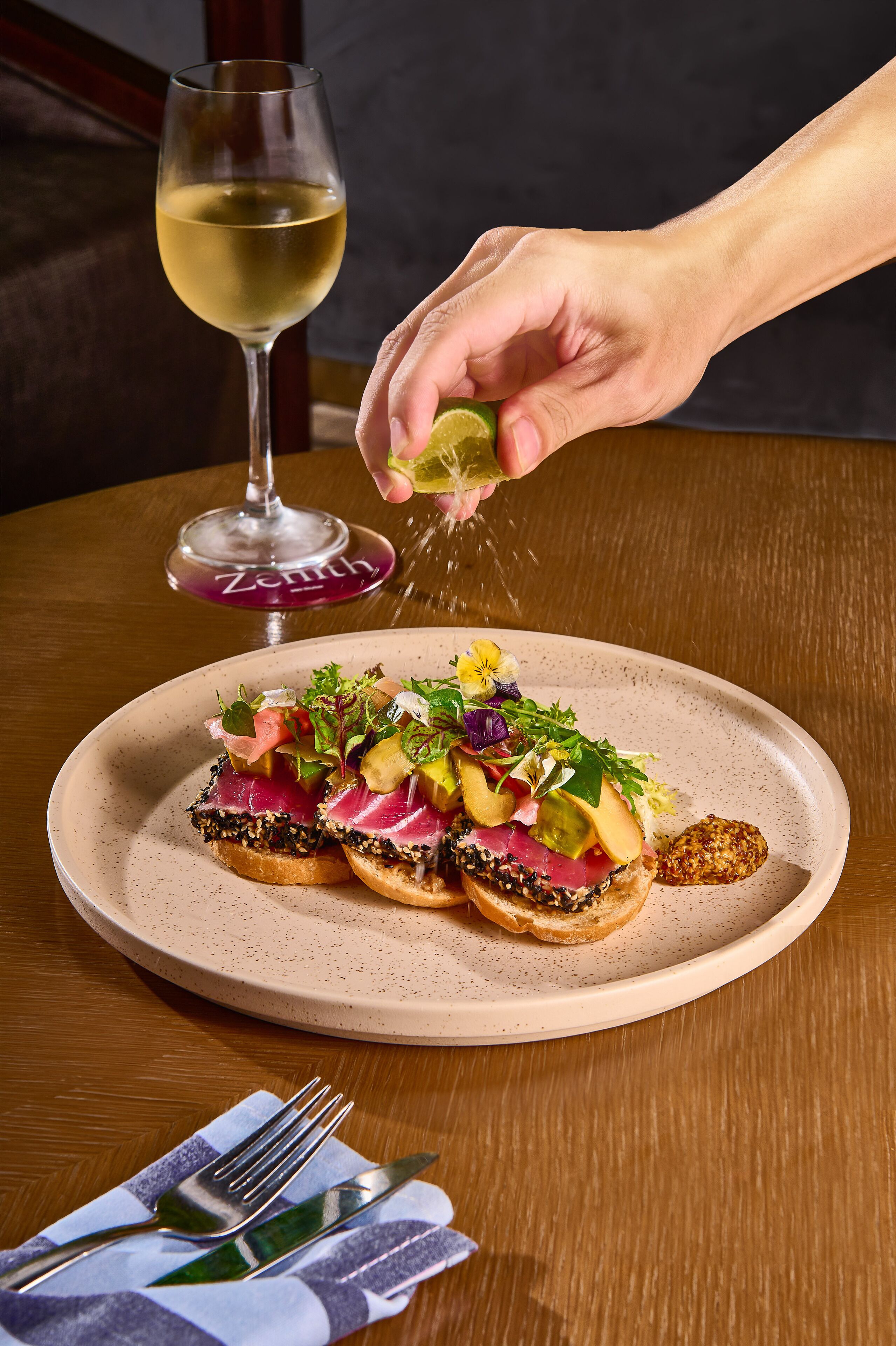 A plate of food with a glass of white wine and a fork on a table.