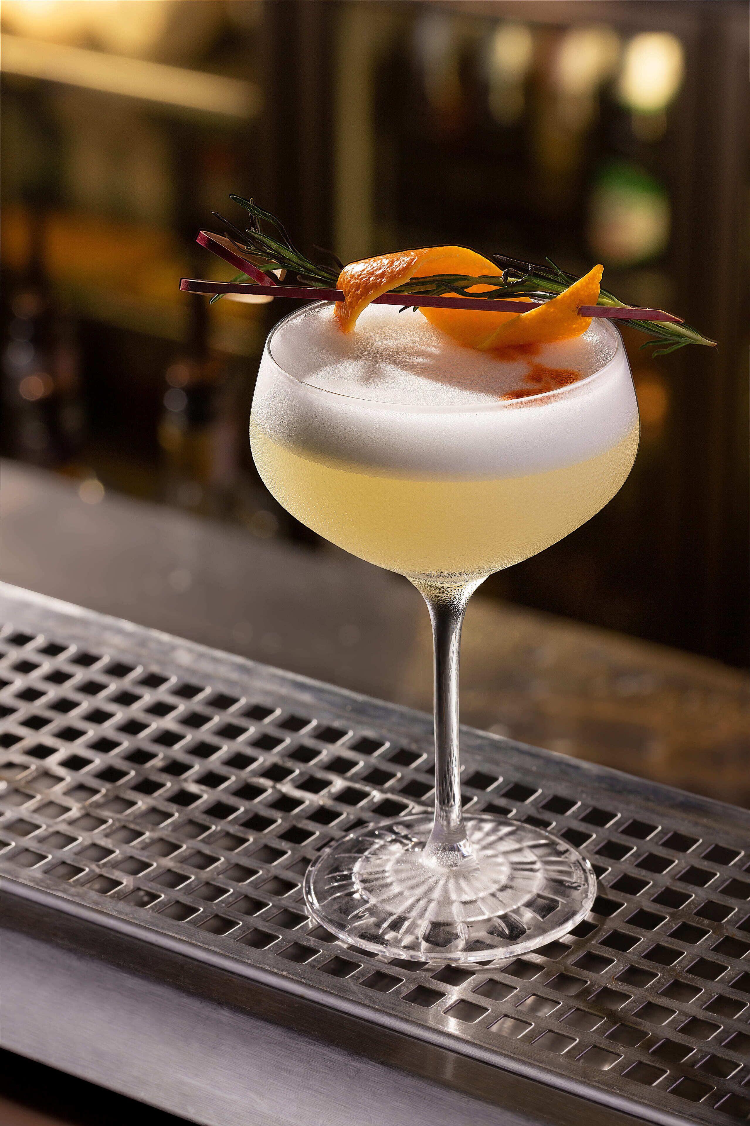 A cocktail in a coupe glass with a garnish on a bar counter.