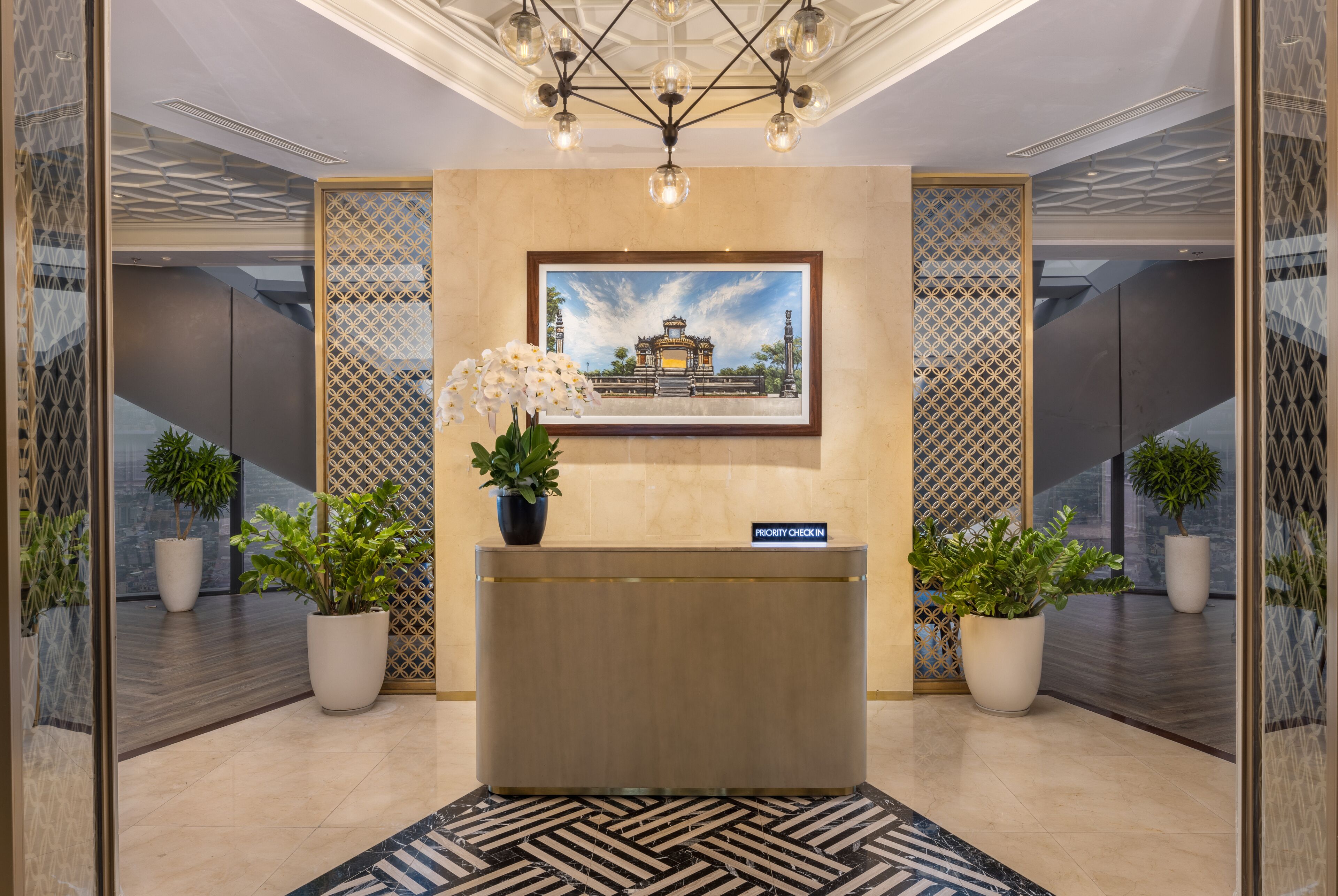 A reception desk with a framed painting, potted plants, and a 'Priority Check-In' sign.