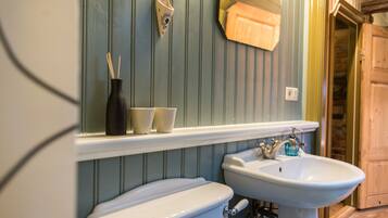 A bathroom with a white toilet, a white sink, and a mirror above the sink. There are two cups on the sink counter and a vase with a plant on the wall.