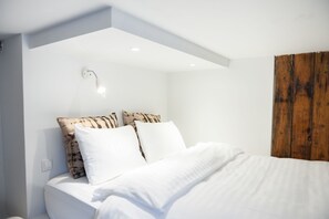A modern bedroom with a bed, white bedding, a wooden headboard, and a wall-mounted light fixture. - Reykjavik Treasure (Reykjavik)