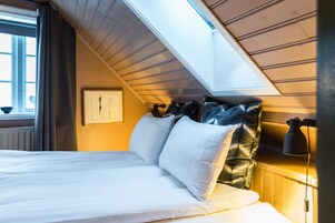 Un dormitorio con techo inclinado, una cama con ropa de cama blanca, un cuadro en la pared y una lámpara de noche.