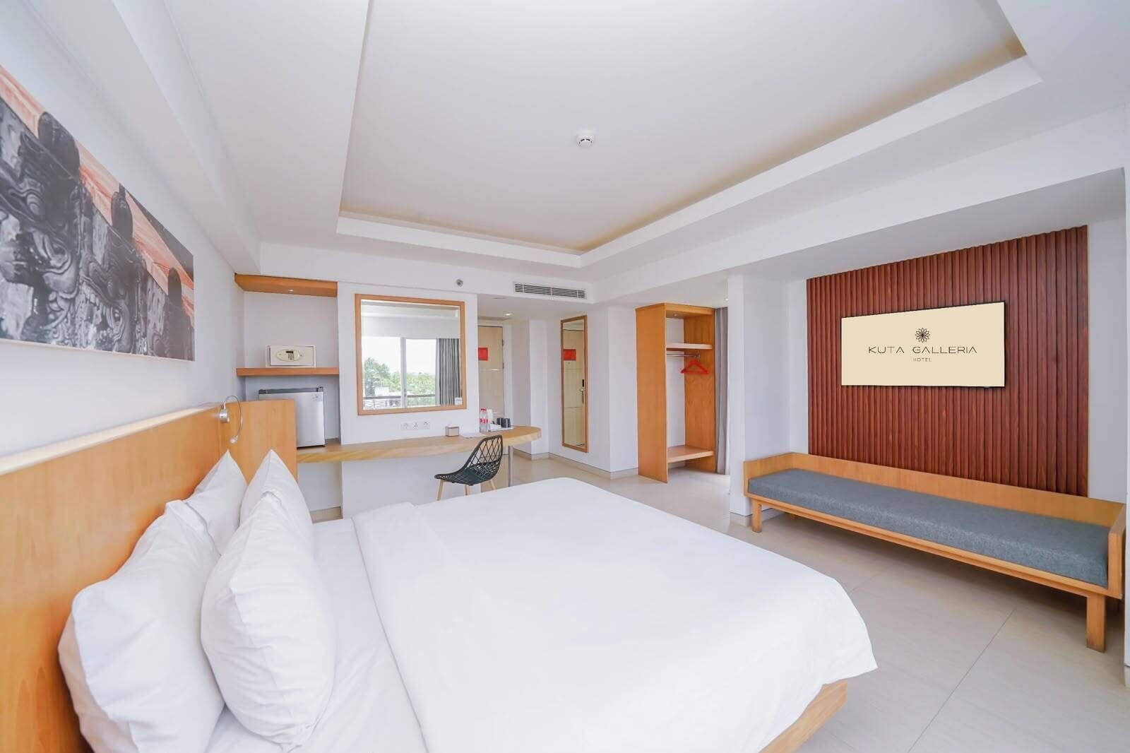 A hotel room with a large bed, a desk, a bench, and a wardrobe.