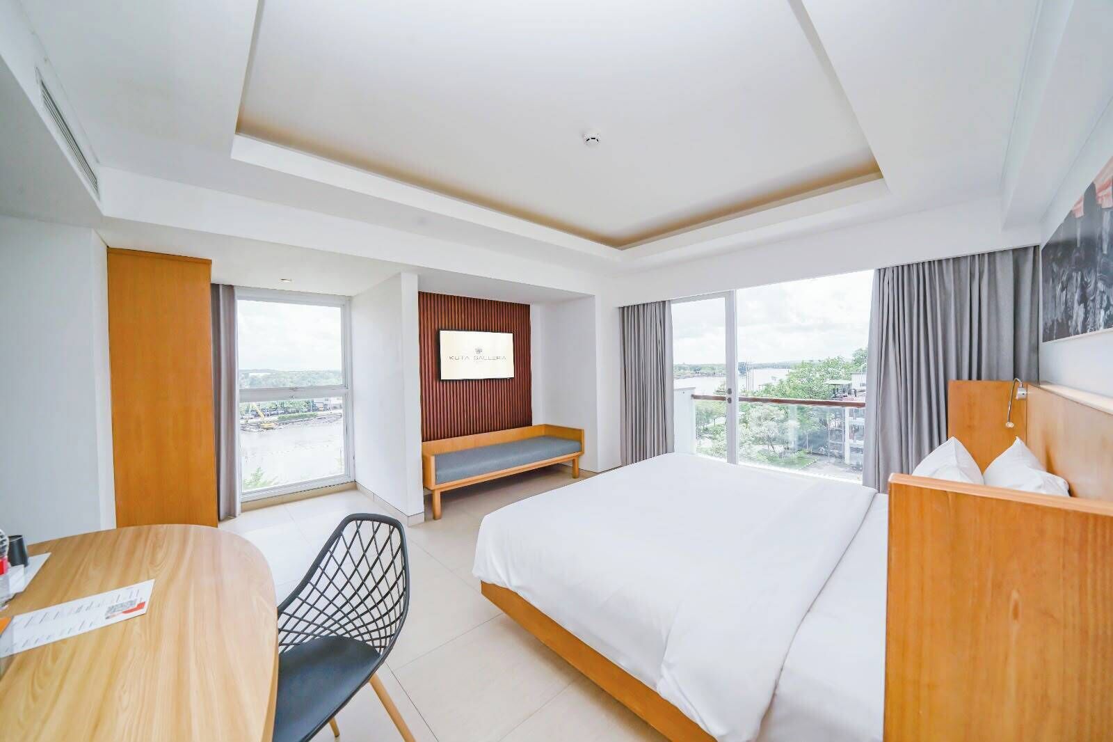 A hotel room with a large bed, a desk, a chair, a TV on the wall, and a balcony with a view.