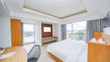 A hotel room with a large bed, a desk, a chair, a TV on the wall, and a balcony with a view.