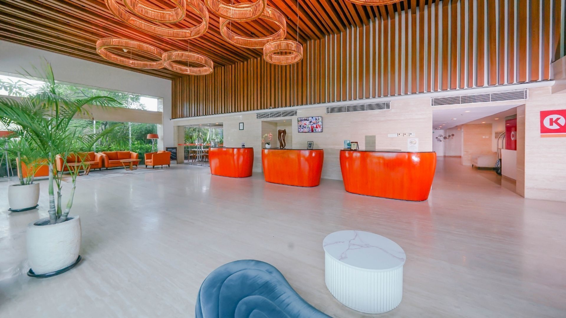 Eine großzügige Lobby mit modernem Design, inklusive einer Rezeption mit orangefarbenen Theken, einem großzügigen Sitzbereich mit orangefarbenen Sofas und einer Decke mit runden Leuchten.
