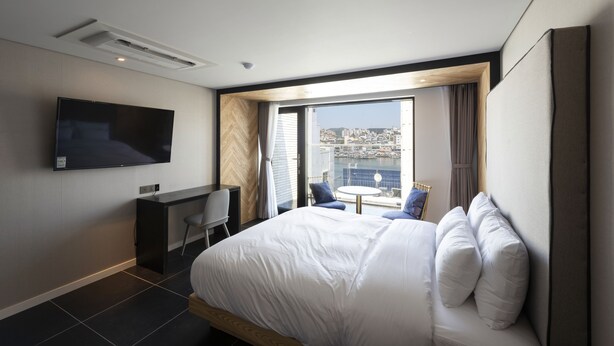 Una habitación de hotel moderna con una cama grande, un escritorio, un televisor de pantalla plana y un balcón con vista a la ciudad.