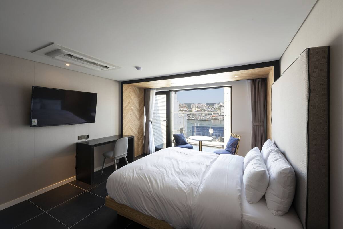 Et moderne hotelværelse med en stor seng, et skrivebord, et fladskærms-tv og en balkon med udsigt over byen.