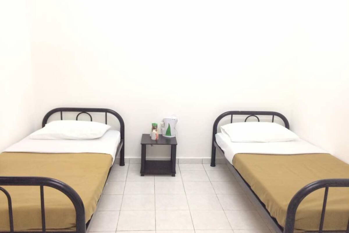 Two single beds with black frames and white bedding, a small black nightstand with a white mug, and a green bottle between the beds.