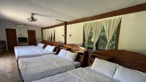 Een hotelkamer met vier eenpersoonsbedden, houten hoofdborden, een plafondventilator en een raam met gordijnen.