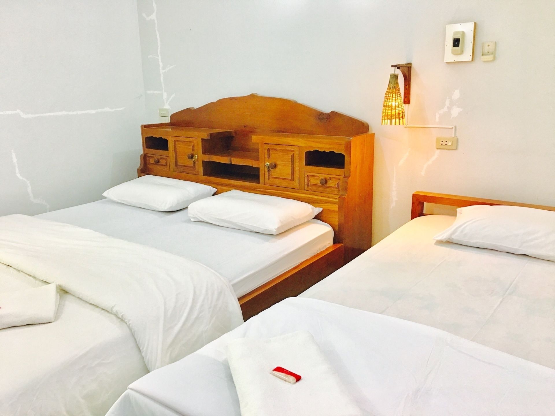 Une chambre avec deux lits simples, chacun doté de draps et d’oreillers blancs. Il y a une tête de lit en bois avec une étagère intégrée et un luminaire fixé au mur au-dessus des lits.