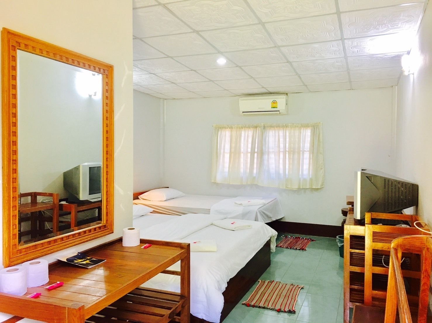 A hotel room with two beds, a wooden desk with a mirror, a television, and a window with curtains.