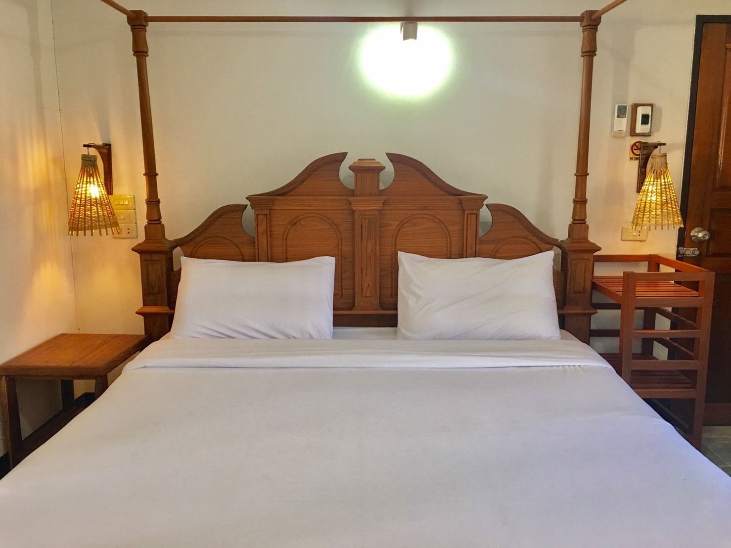 Una cama con dosel con ropa de cama blanca, cabecera de madera y dos mesitas de noche con lámparas.