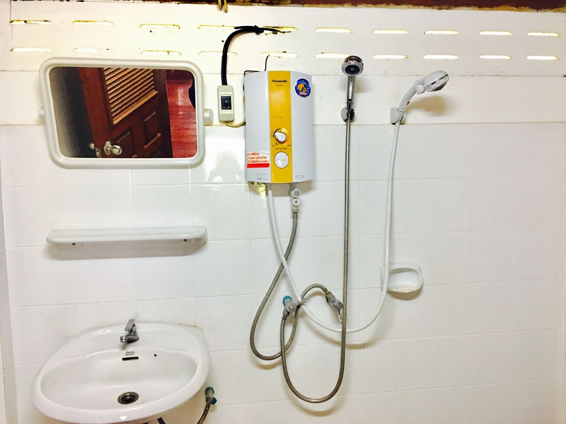 Un baño con un lavamanos blanco, un espejo, un cabezal de ducha de mano y un calentador de pared.