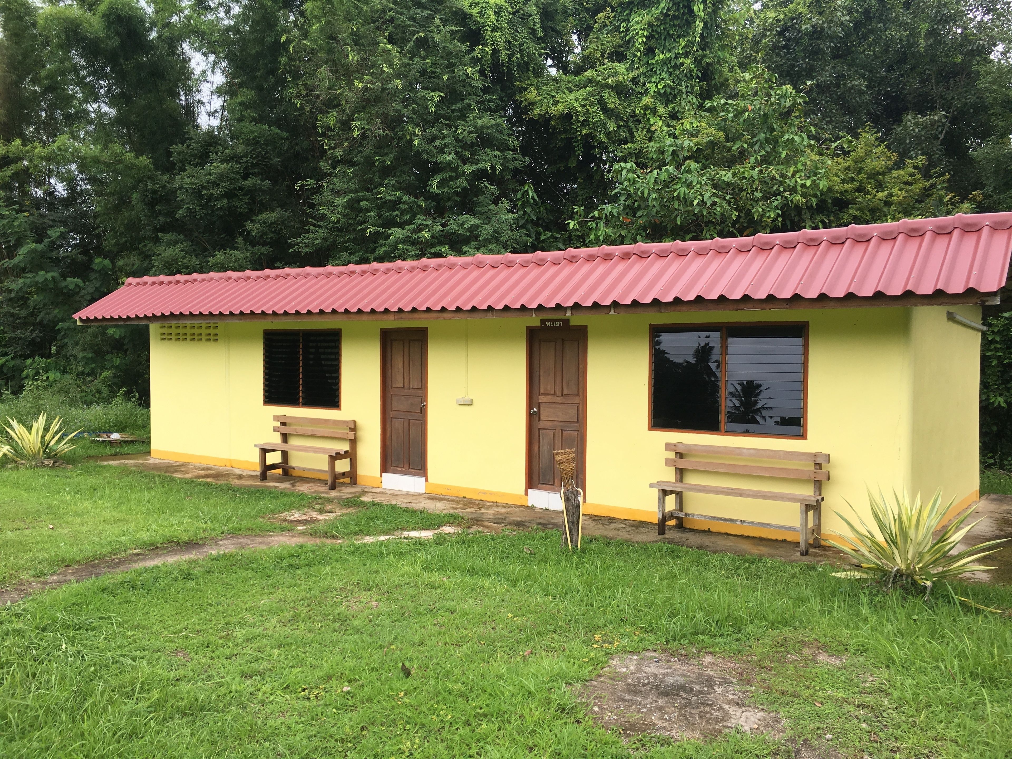 A small yellow building with a red roof, two wooden benches, and a door.
