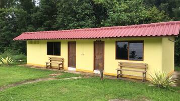 A small yellow building with a red roof, two wooden benches, and a door.
