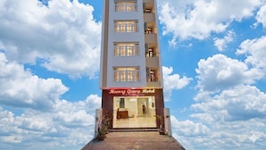 Een hotel met meerdere verdiepingen, met een heldere lucht en wolken op de achtergrond.