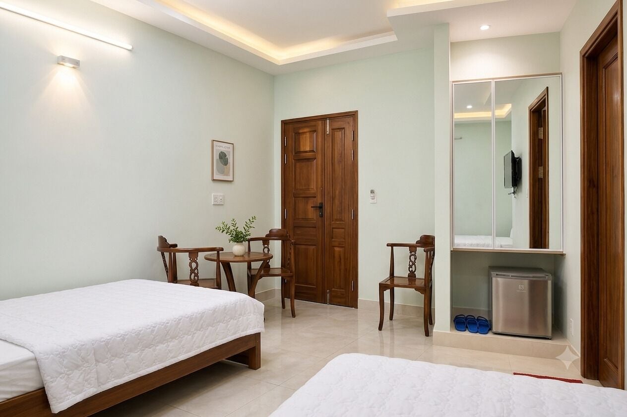 A bedroom with two beds, a wooden door, a small table with chairs, a mirror, and a mini-fridge.