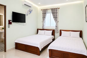 Une chambre d’hôtel avec deux lits en bois, un téléviseur à écran plat, un climatiseur, un téléphone et une fenêtre avec des rideaux.