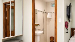 Een badkamer met een douche, wastafel en een spiegel. Op de vloer ligt een rood kleed en er staat een klein mandje.