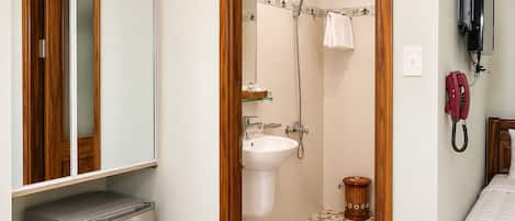 Un baño con ducha, lavabo y espejo. Hay una alfombra roja en el suelo y una pequeña cesta.