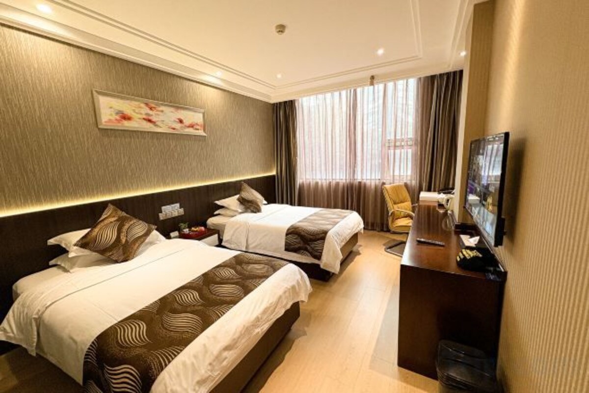 A hotel room with two beds, a desk, a chair, a TV, and a window with curtains.