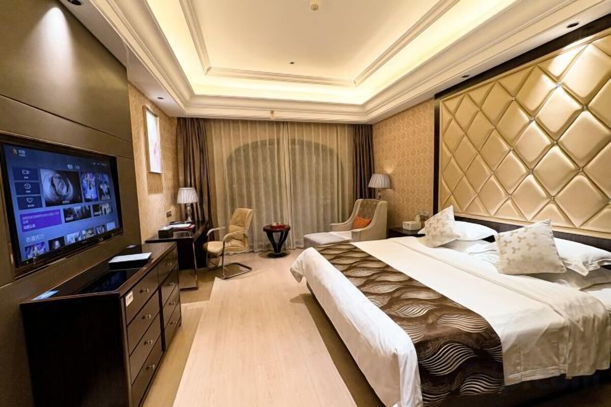 A hotel room with a large bed, a television, a desk, and a chair.