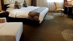 A hotel room with a large bed, a desk with a lamp, a chair, and a decorative rug. - Bojue Hotel (Jiaxing)
