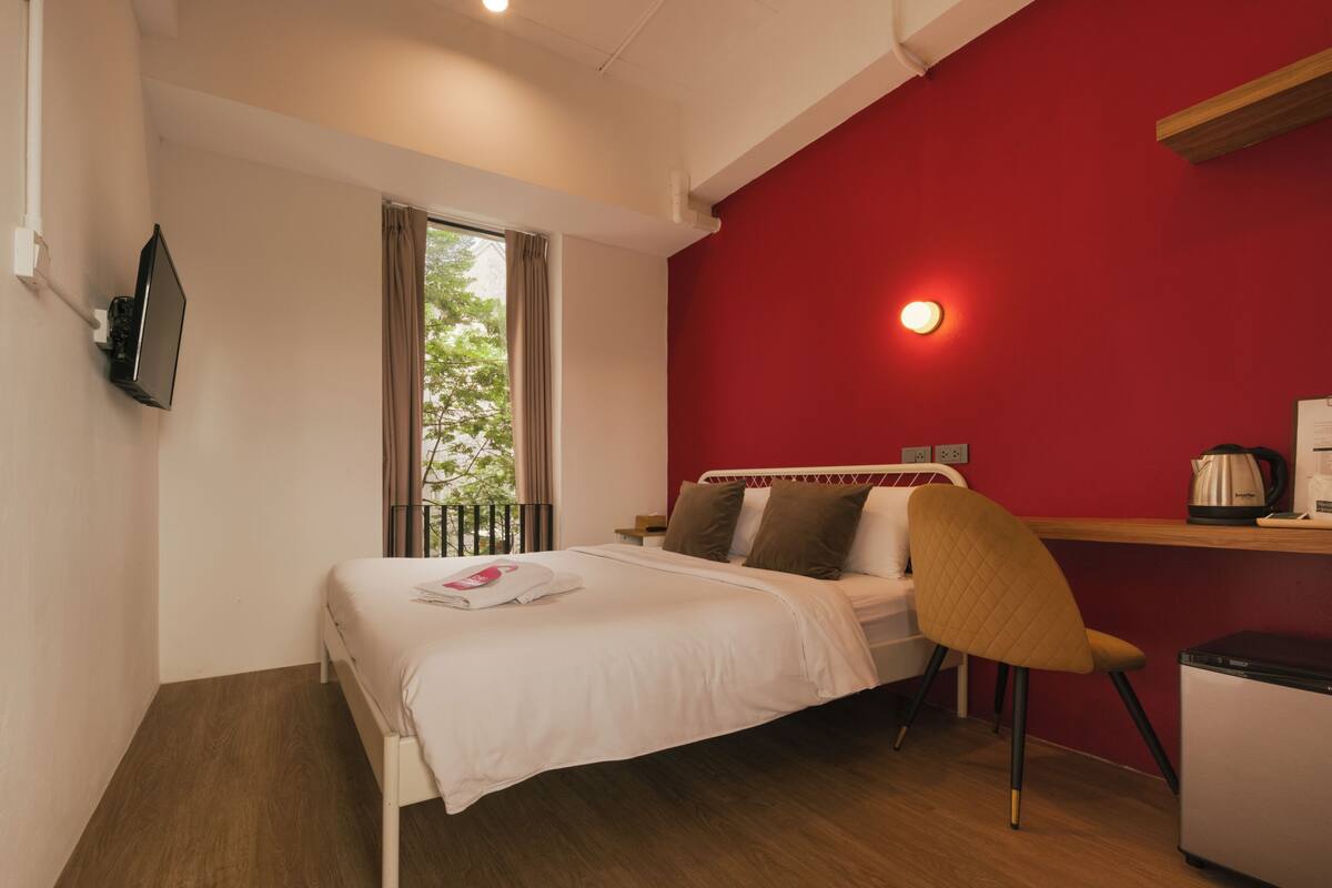 Een hotelkamer met een bed, een stoel, een bureau met een waterkoker en een aan de muur bevestigde televisie.