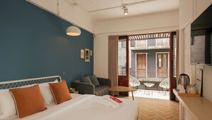 Ein Hotelzimmer mit Bett, einer Couch, einem kleinen Tisch und einem Balkon mit Blick auf Gebäude.
