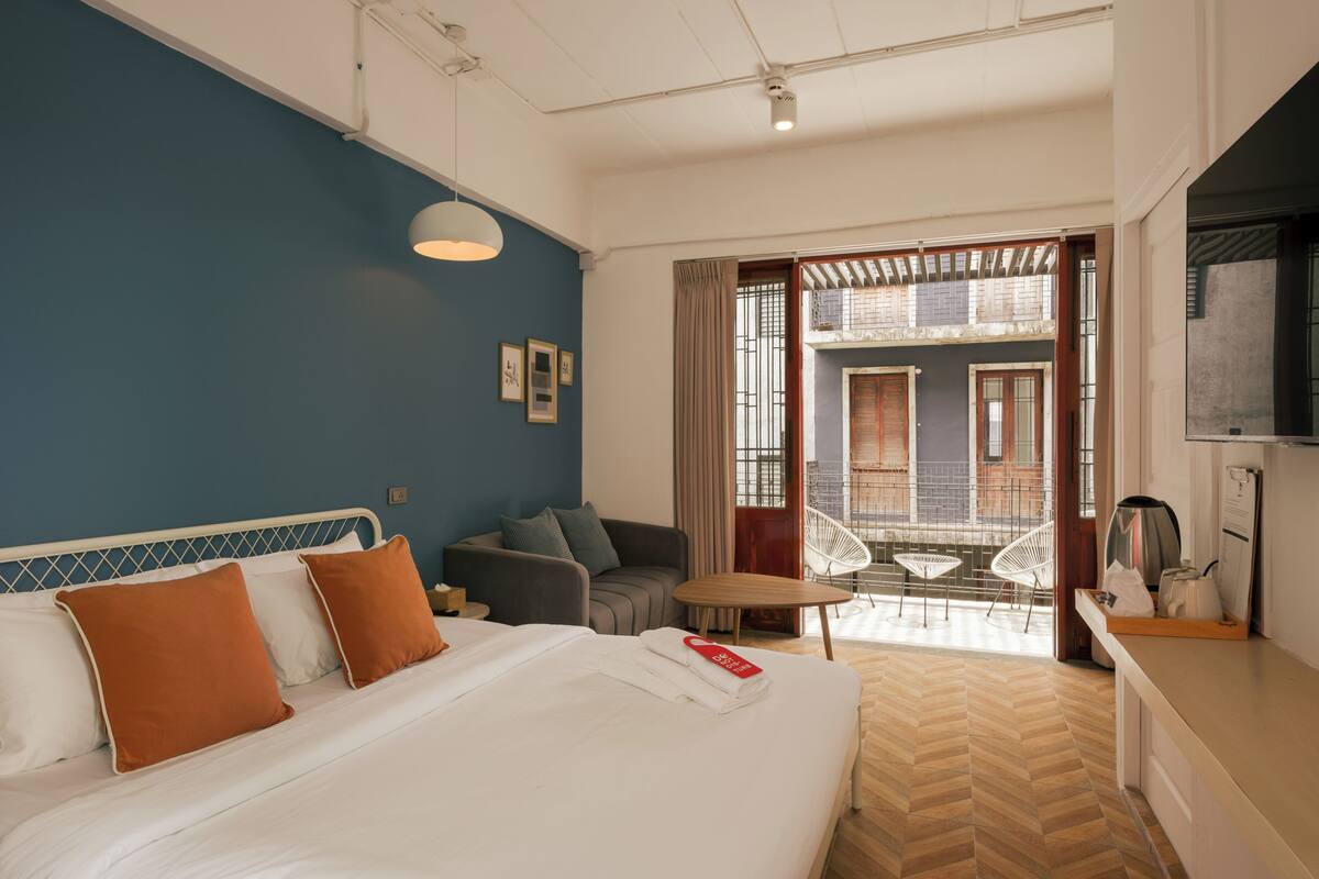 Een hotelkamer met een bed, een slaapbank, een tafeltje en een balkon met uitzicht op gebouwen.