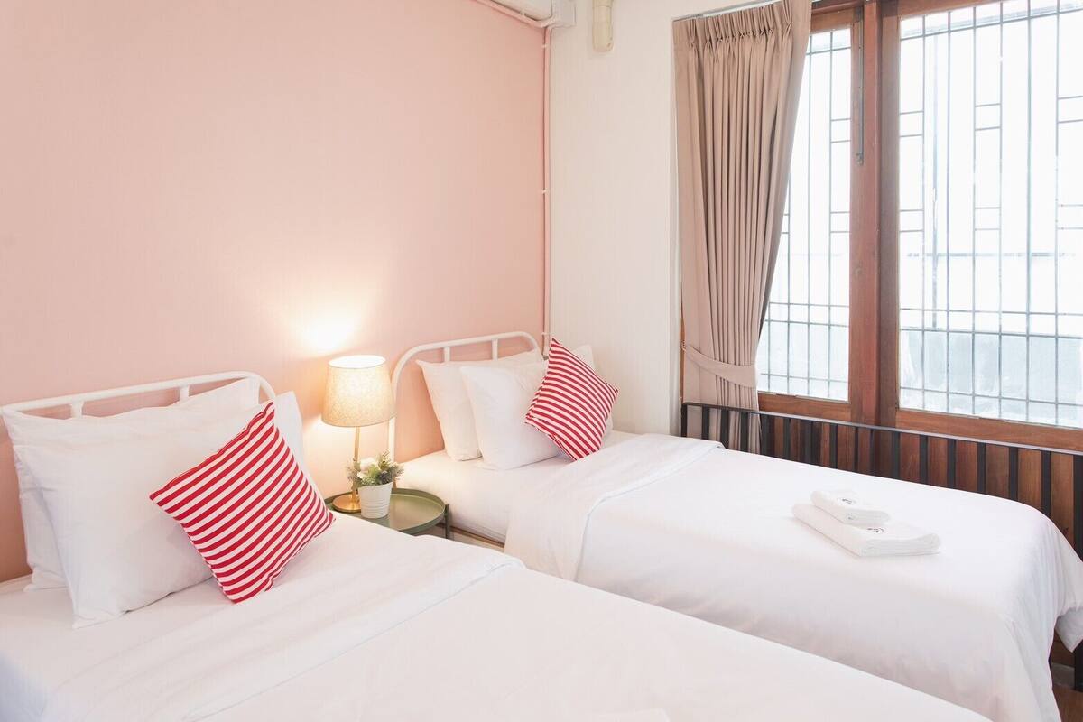Een hotelkamer met twee bedden, een nachtkastje met een lamp, een raam met gordijnen en een radiator.