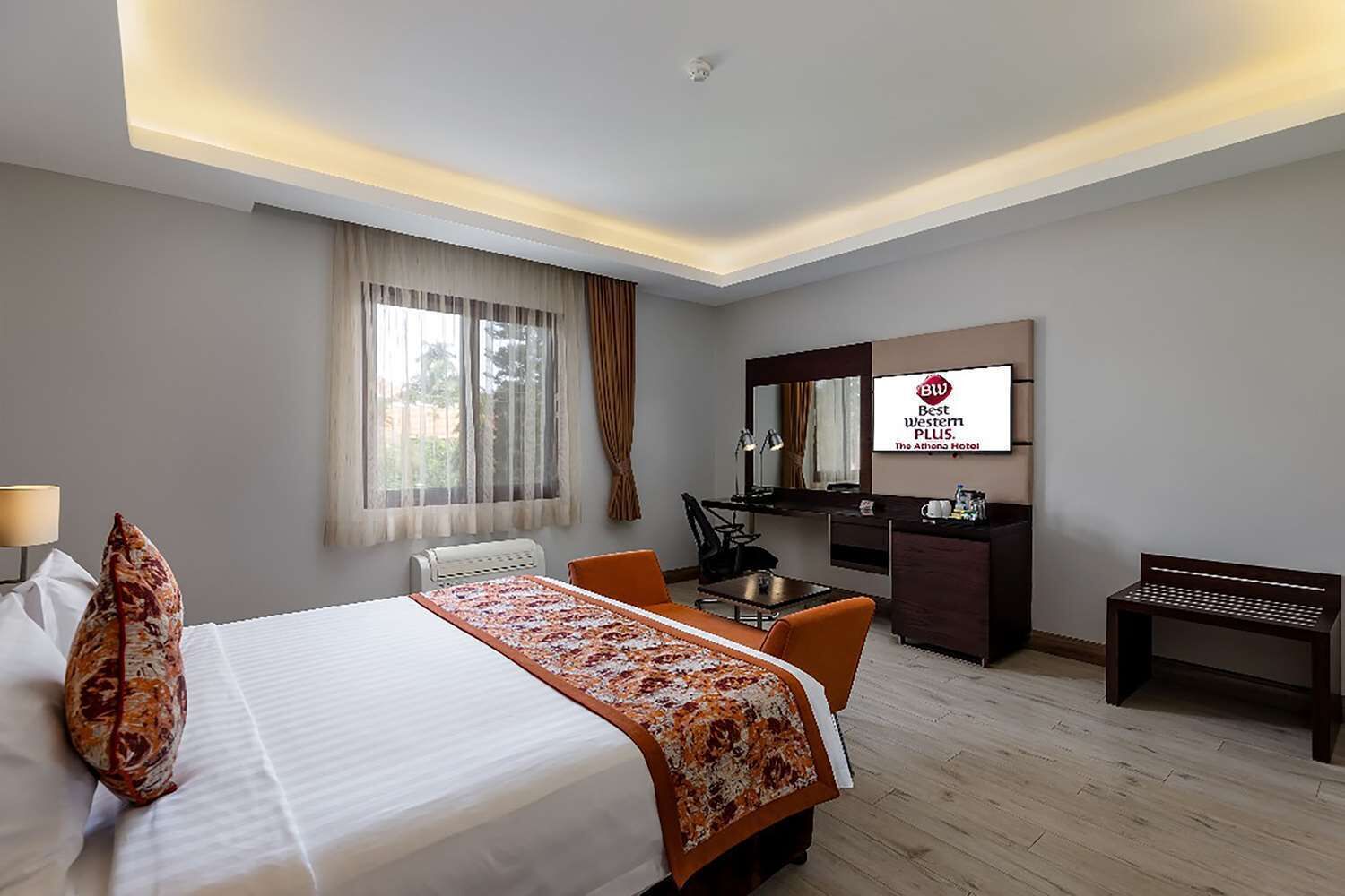 A hotel room with a bed, desk, chair, and a television displaying the hotel's logo.