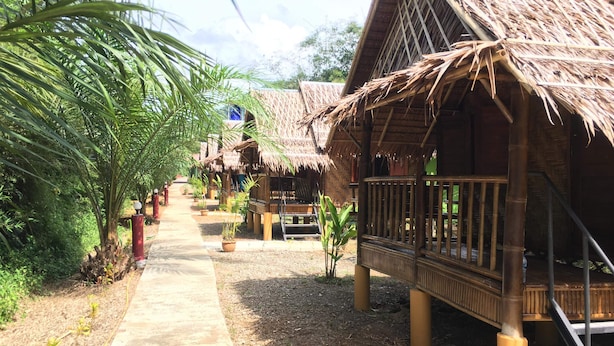 Un sentier mène à des huttes aux toits de chaume, de part et d’autre, un jardin tropical s’y trouve.