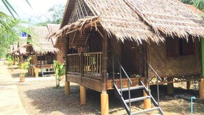 Une hutte traditionnelle à toit de chaume, dotée d’un porche en bois et d’un escalier menant à l’entrée.