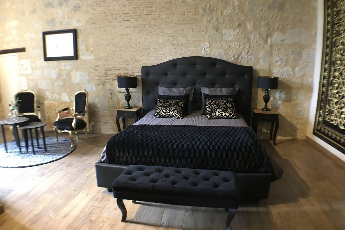 Ein Schlafzimmer mit einem großen Bett, zwei Nachttischen, einem Sessel und einem kleinen runden Tisch.
