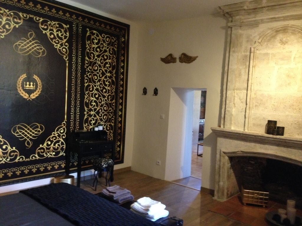 Una habitación con un gran panel decorativo negro y dorado, una chimenea y una cama con cubierta azul oscuro.